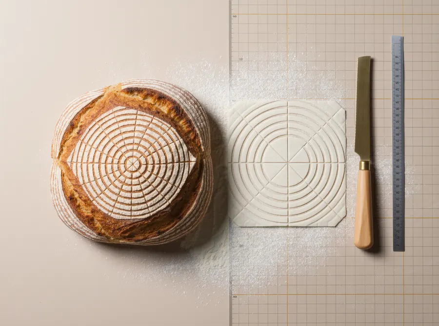 a loaf with a precise geometric flour pattern, a stencil, a knife and a ruler on a cutting mat